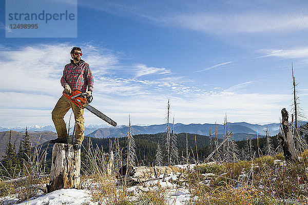 Mann mit Kettensäge auf Baumstumpf stehend beim Camping in Montana