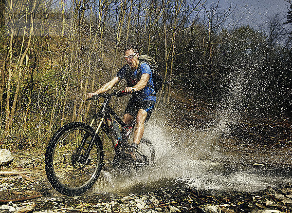 Ein Mann fährt mit seinem Mountainbike über einen Gebirgsbach. Das Bild wurde im Moment des größten Wasserschadens aufgenommen. Aufgenommen im Gledic-Gebirge in der Nähe von Kragujevac  Zentralserbien  an einem sonnigen Frühlingstag.'