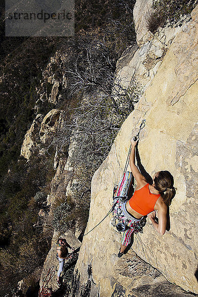 Eine Frau mit rotem Tanktop und gestreifter Hose klettert The Rapture (5.8) am Lower Gibraltar Rock in Santa Barbara  Kalifornien. The Rapture ist eine sehr schöne und unglaublich gut abgesicherte Route auf der linken Seite des Lower Gibraltar Rock.