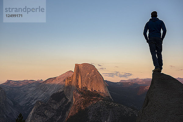 Mann auf einem Felsen stehend mit Blick auf den Half Dome im Licht des Sonnenuntergangs. Yosemite  CA  USA.
