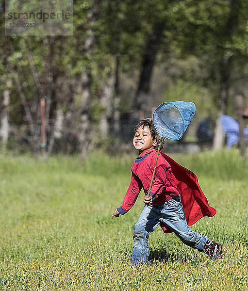 Junger asiatischer Junge jagt Schmetterlinge auf grasbewachsener Landschaft