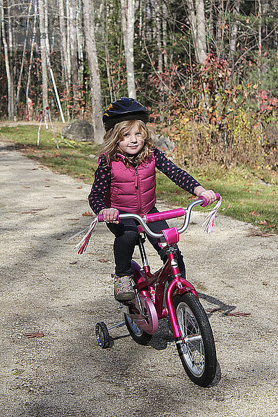 Ein junges Mädchen fährt auf einem rosa Fahrrad mit Stützrädern