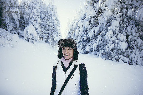 Porträt einer im Wald stehenden Frau im Schnee