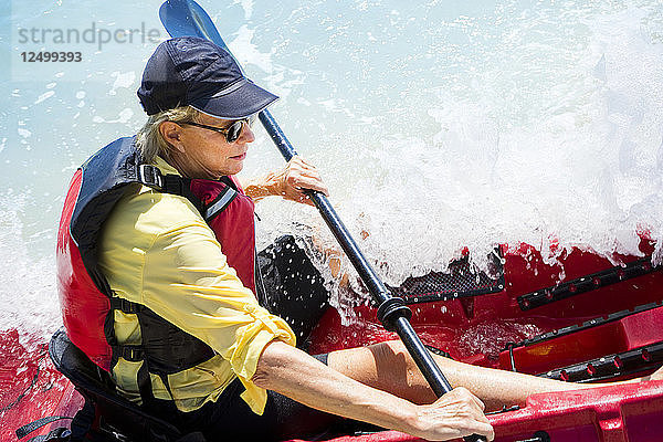 Frau in einem Kajak mit einer Welle  die über das Boot bricht