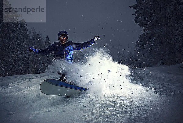 Snowboarder in einer Kurve im Tiefschnee auf dem Berg Goc  Serbien. Aufnahme beleuchtet mit Blitzlicht.