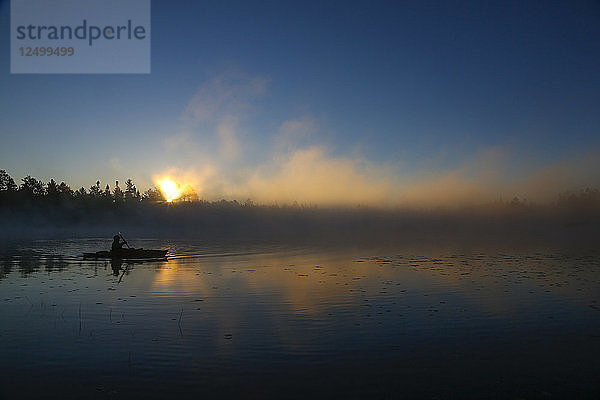 Ein Kajakfahrer genießt den Sonnenaufgang  während an einem kühlen Herbstmorgen Dampf aus dem Lake Pleasant in Conover  Wisconsin  aufsteigt.