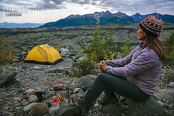 Frau sitzt bei einem Lagerfeuer über dem Root-Gletscher in Alaska  USA