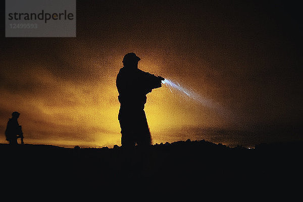 Silhouette einer Person in Militäruniform mit Waffe und Taschenlampe