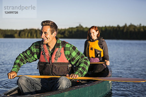 Ein junges Paar paddelt ein Kanu durch Morgennebel auf Long Pond in der Nähe von Greenville  Maine