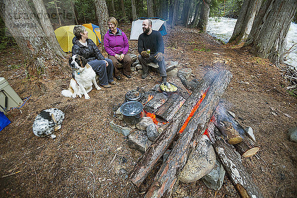 Drei Camper sitzen am Lagerfeuer und warten auf ihre Mahlzeit