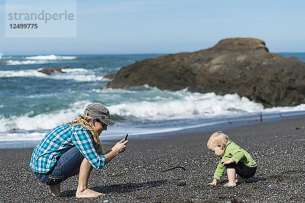 Eine Mutter macht ein Smartphone-Foto von ihrer kleinen Tochter  die am Strand spielt. Kalifornische Küste