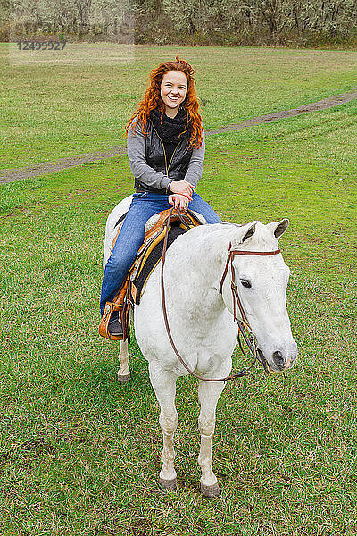 Porträt eines reitenden Mädchens mit roten Haaren und einem weißen Pferd auf einem öffentlichen Reitgelände.