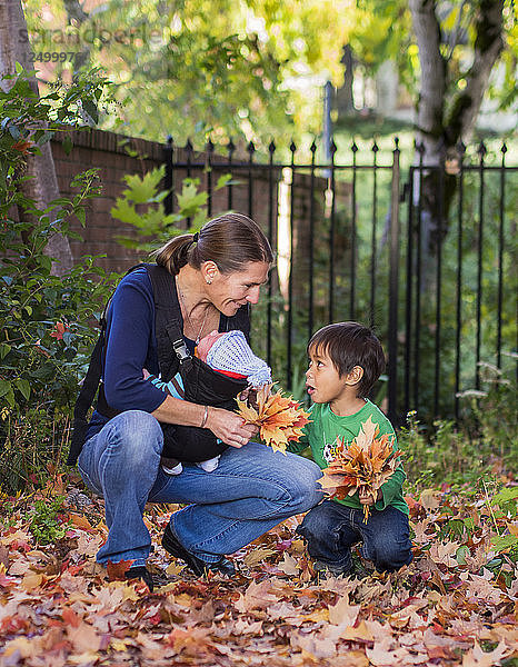 Mutter mit Baby spielt mit kleinen Jungen im Herbst Blätter