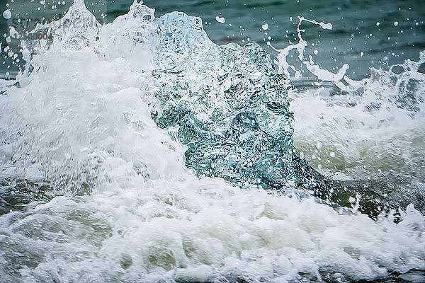 Wellen brechen über einen größtenteils geschmolzenen Eisberg am Strand von Jokulsarlon  Island