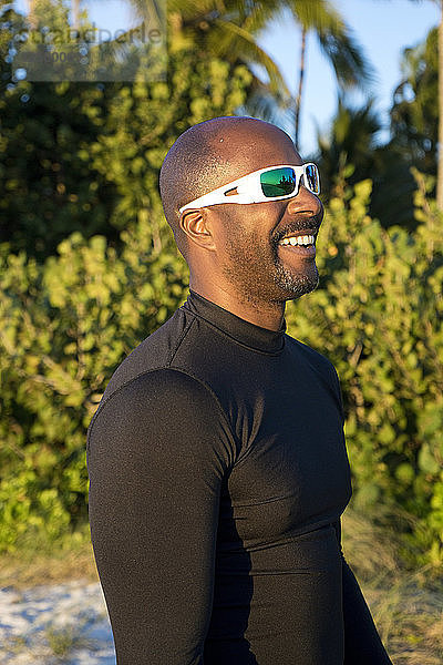 Sportlicher Mann lachend  mit Sonnenbrille  in einer tropischen Umgebung