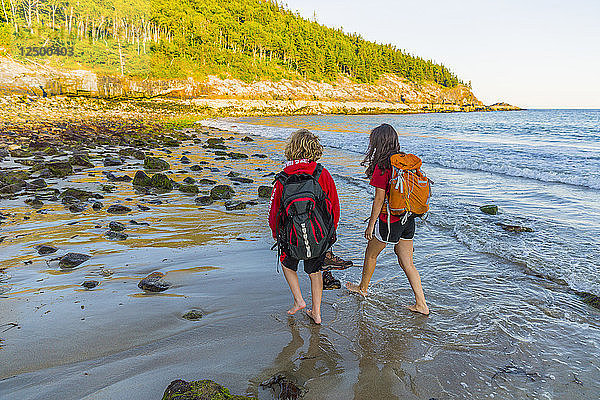 Jugendlicher Junge und Mädchen gehen barfuß am Strand im Acadia National Park spazieren