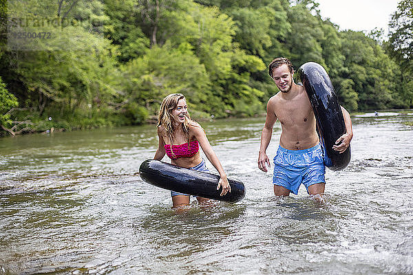 Ein junger Mann und eine Frau unterhalten sich und lachen  während sie mit Schläuchen einen Fluss hinuntergehen.