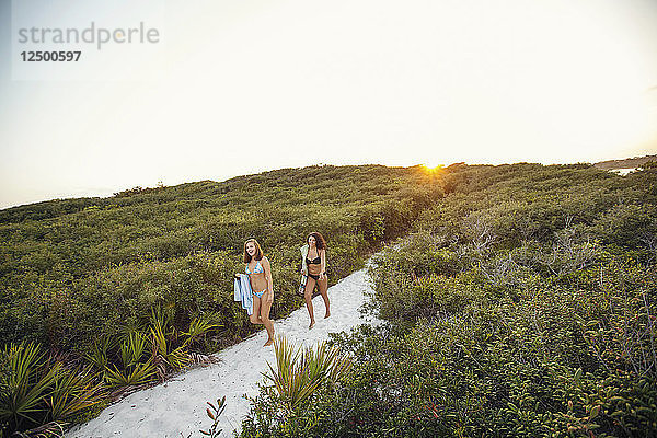 Zwei junge Frauen wandern auf Pfaden durch eine Sanddüne an einem Strand in Florida.
