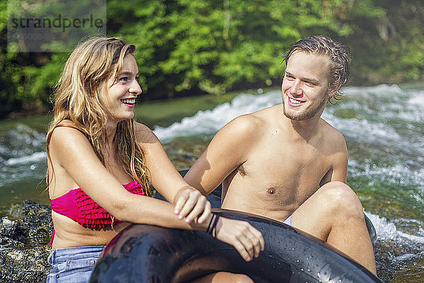 Ein junger Mann und eine Frau lächeln  während sie sich auf einem Wasserfall ausruhen  nachdem sie einen Fluss hinuntergerutscht sind.