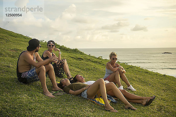 Eine Gruppe von Freunden entspannt sich auf einer Wiese an der Küste