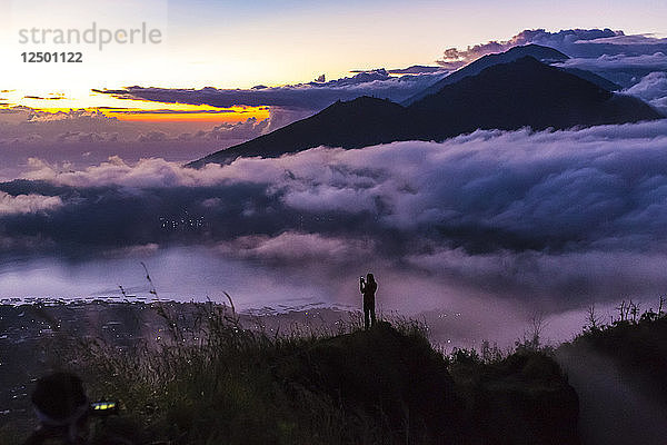 Mann fotografiert mit Smartphone in den Bergen bei Sonnenaufgang