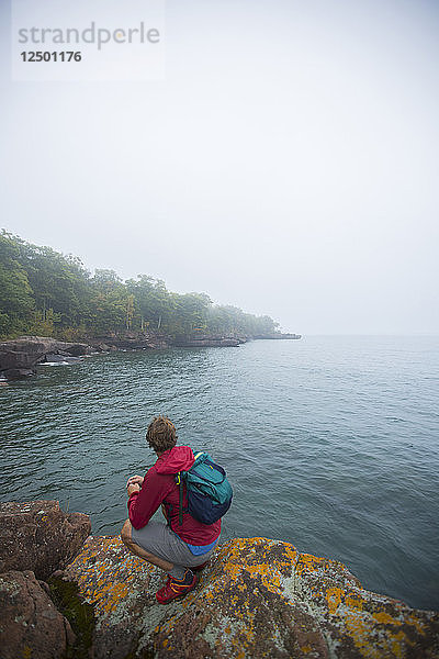 Männlicher Wanderer auf einem Felsen beim Erkunden des Lake Superior in Wisconsin