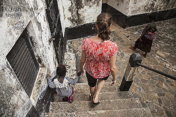 Frau geht mit einem kleinen ghanaischen Kind die Treppe einer Festungsruine in Axim  Ghana  hinunter.