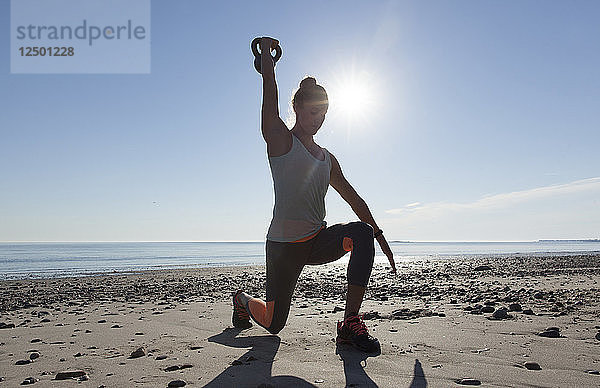 Frau macht Übung am Strand mit Kettlebell