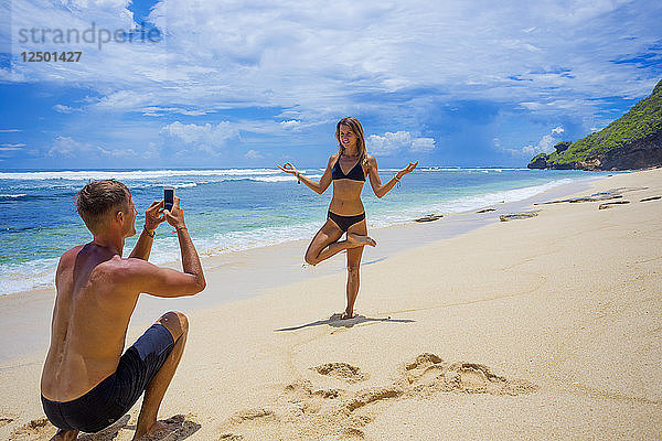 Junger Mann macht ein Foto von einer hübschen Frau am Strand.
