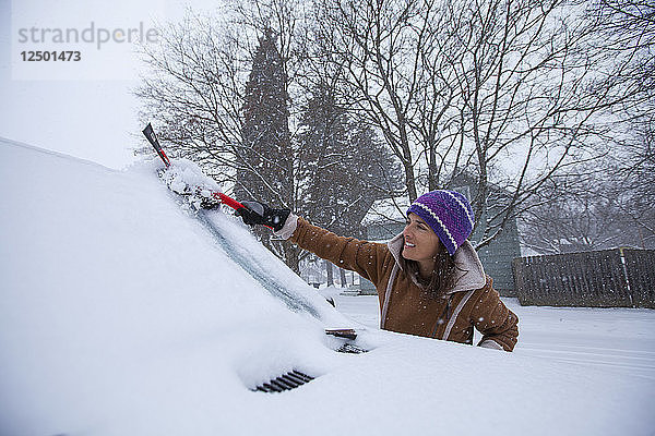 Eine erwachsene Frau  die ihre Windschutzscheibe nach einer frischen Schneedecke abräumt
