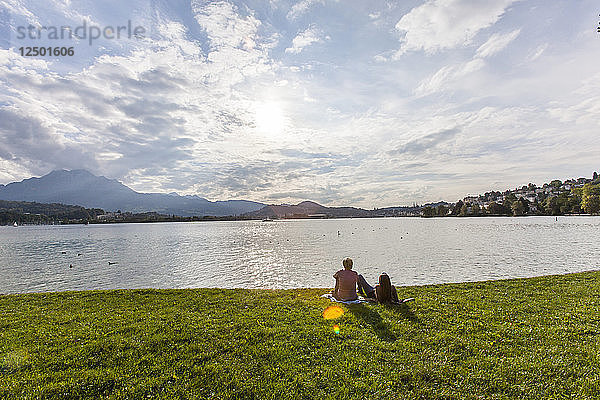 Ein Paar sitzt im Gras am Ufer des Vierwaldstättersees in der Schweiz und blickt auf die nahe gelegenen Berge Rigi und Pilatus sowie die Alpen.