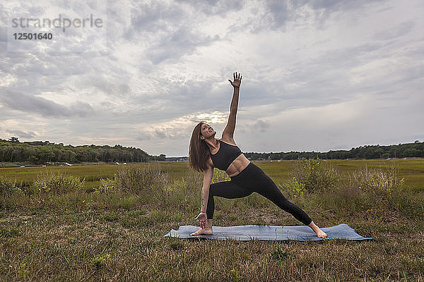 Schöne junge Frau streckt sich zum Himmel und macht Yoga bei Sonnenuntergang