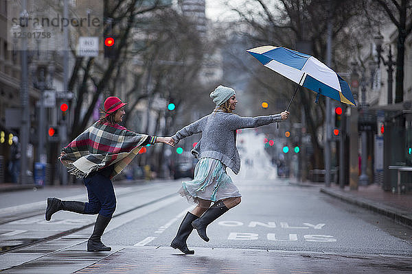 Zwei Frauen laufen über eine Straße und halten sich an den Händen und einen Regenschirm. Portland  Oregon.