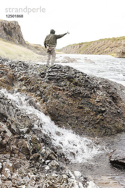 Mann wirft beim Fliegenfischen am Fluss Nor??ur?°  Island  neben einer kleinen heißen Quelle.