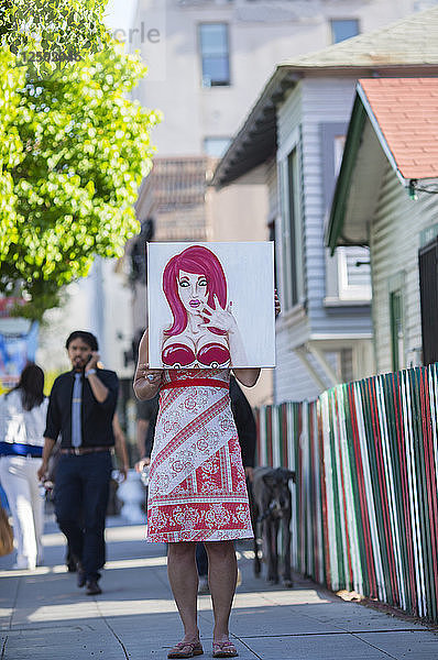 Eine Frau hält in San Diegos Little Italy ein kaputtes Gemälde vor sich.