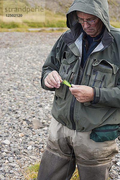 Älterer Mann bei der Auswahl von Fliegenfischerfliegen während eines Ausflugs zum Fluss Nor??ur?°  Island.