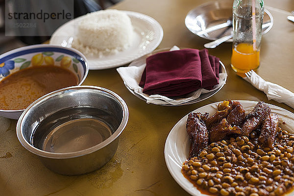 Typisches Mittagessen in Accra  Ghana  bestehend aus Reis  Bohnen  rot-rot  Huhn und einer Wasserschüssel zum Händewaschen.