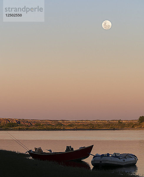 Ein Treibboot und ein aufblasbares Floß am Flussufer bei Sonnenuntergang. Fluss Limay Medio  Patagonien  Argentinien. Der Vollmond ging über dem Horizont auf.