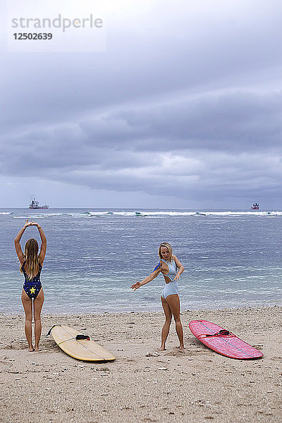 Zwei junge Frauen strecken und beugen sich vor dem Surfen am Strand