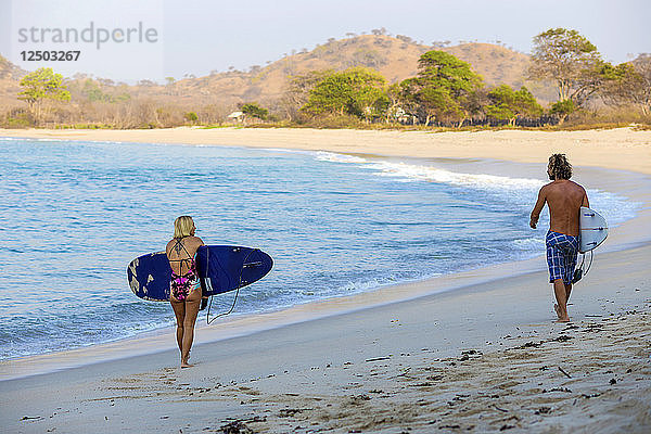 Surfer mit Brettern laufen an der Küste entlang. West Sumbawa.Indonesien.Indonesien