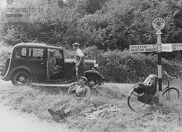 Menschen  die sich an einem Wegweiser mit einem Standard-10-PS-Auto von 1935 ausruhen  Devon  (um 1935?). Künstler: Unbekannt