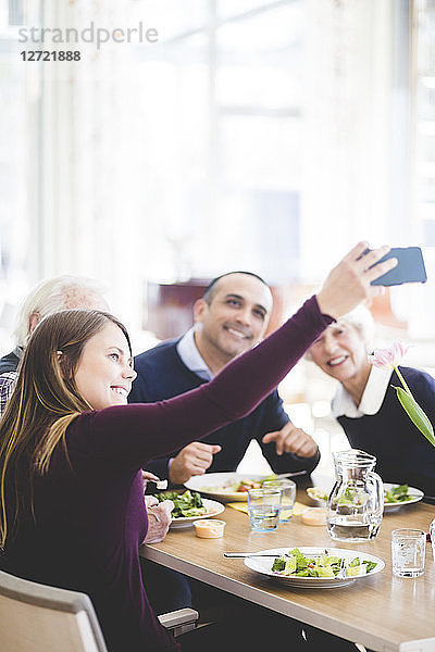 Young woman taking selfie with father and grandparents while having lunch in nursing home
