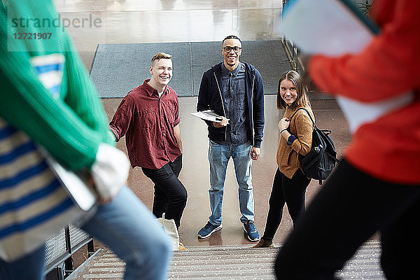 Smiling friends looking at female university students on steps while standing in corridor