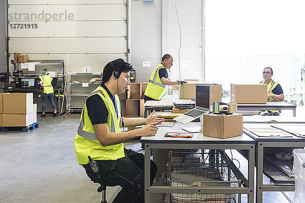 Young customer service representative talking through headset while coworkers at warehouse