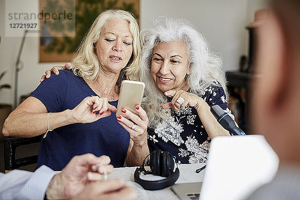 Senior woman showing mobile phone to friend while vlogging at home