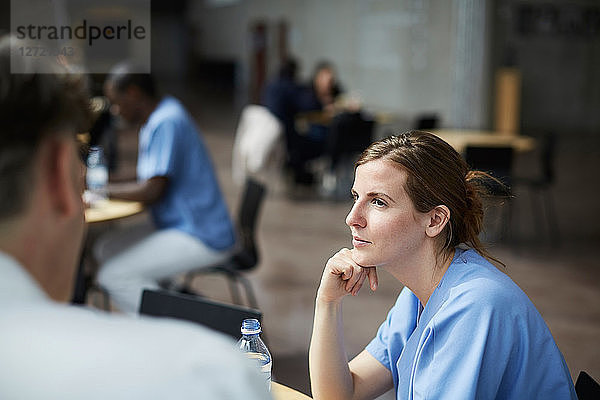 Confident female nurse looking at mature doctor while sitting in hospital cafeteria