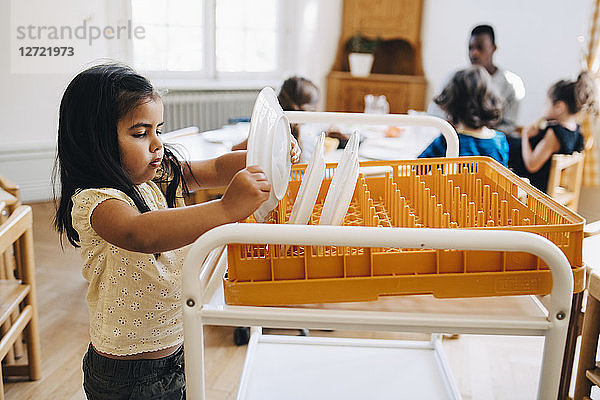 Side view of girl placing plate in crate on cart in classroom