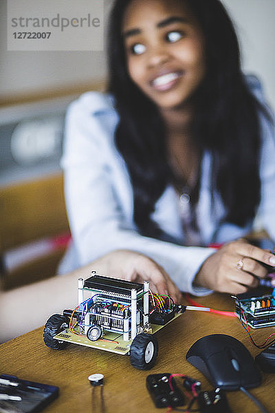 Smiling student sitting by friend with toy car on desk in classroom at high school