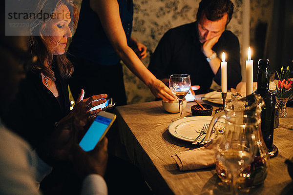 Mature friends using mobile phones while sitting at dining table in dinner party