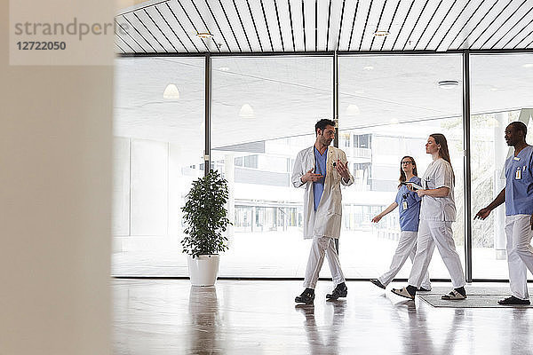 Full length of doctors and nurses discussing while walking in corridor against window at hospital